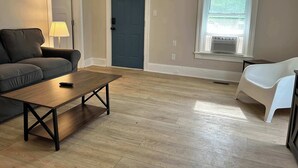 A living room with a sofa, a coffee table, a lamp, a door, and a window with blinds. - Elm Corner, 2 bedroom family house in Historic Loveland (Loveland)