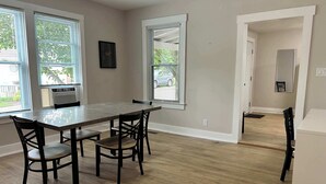 A dining area with a wooden table and chairs, large windows with blinds, and a view of the outside. - Elm Corner, 2 bedroom family house in Historic Loveland (Loveland)