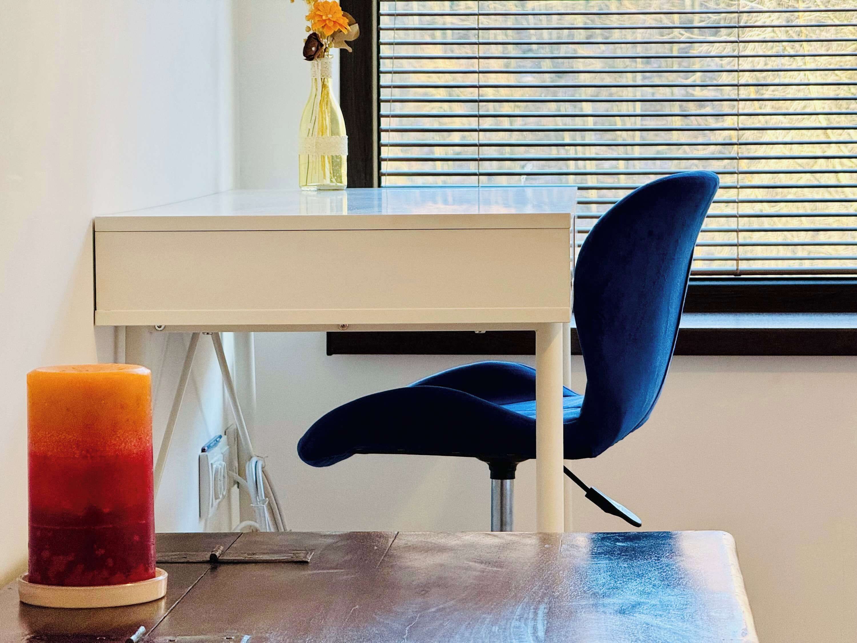Una habitación moderna con una mesa de vidrio, una silla azul y una vela.
