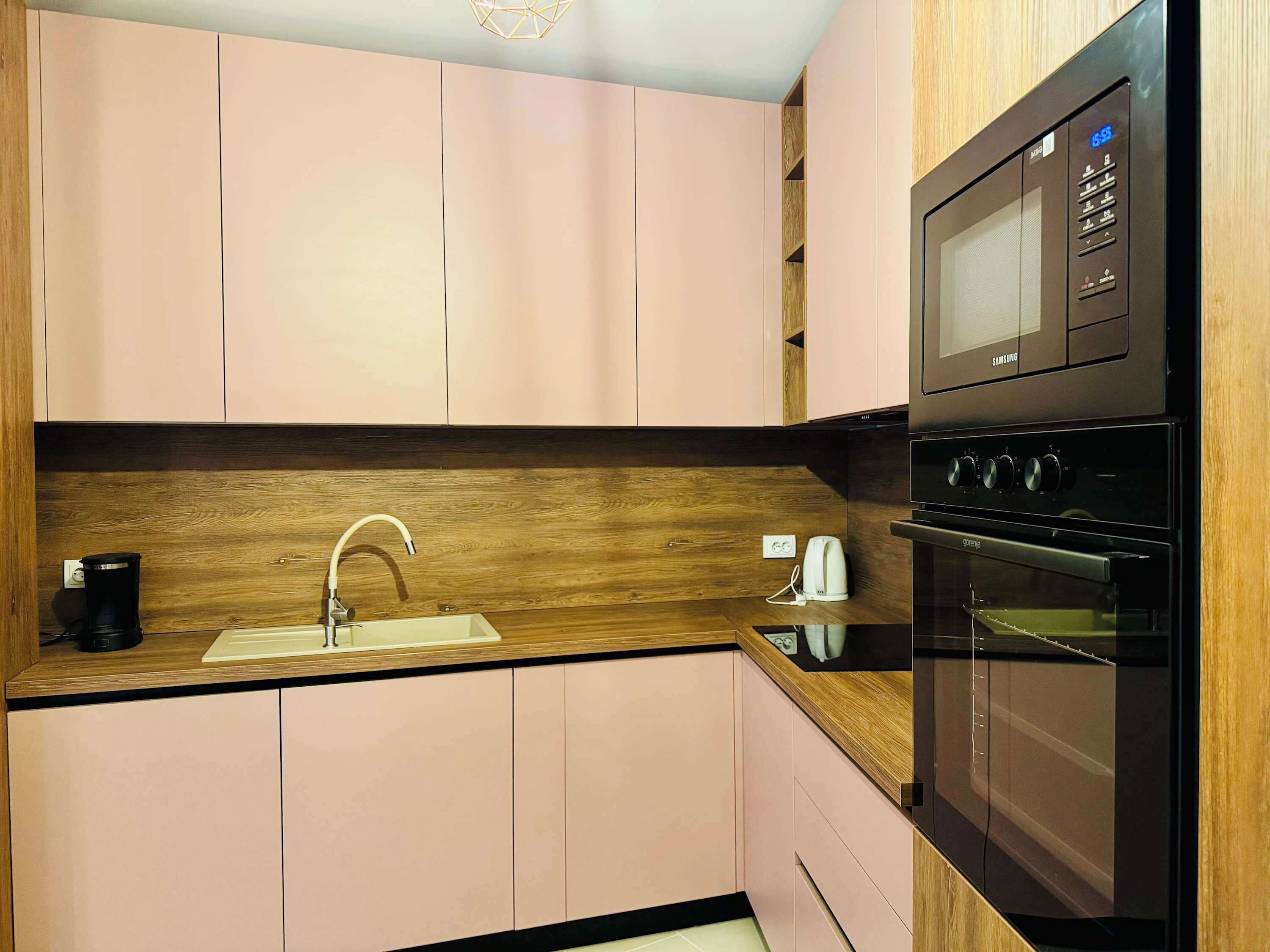 A modern kitchen with pink cabinets, a wooden countertop, a built-in microwave, and an oven.