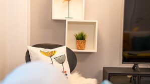 A living room with a modern design, featuring a black chair with a white cushion, a small shelf with a plant, and a television on a black stand. - Joy City Stay Madgearu 2 (Timișoara)