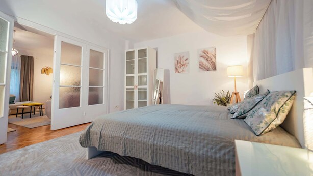 A modern bedroom with a large bed, a white wardrobe, and a dining area with a table and chairs. - Joy City Stay Madgearu 2 (Timișoara)