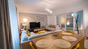 A modern living room with a sofa, TV, and dining area with yellow chairs and a wooden table. - Joy City Stay Madgearu 2 (Timișoara)