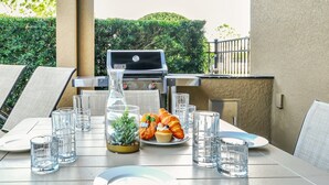 Un patio al aire libre con una parrilla, asientos y una mesa lista para una comida.