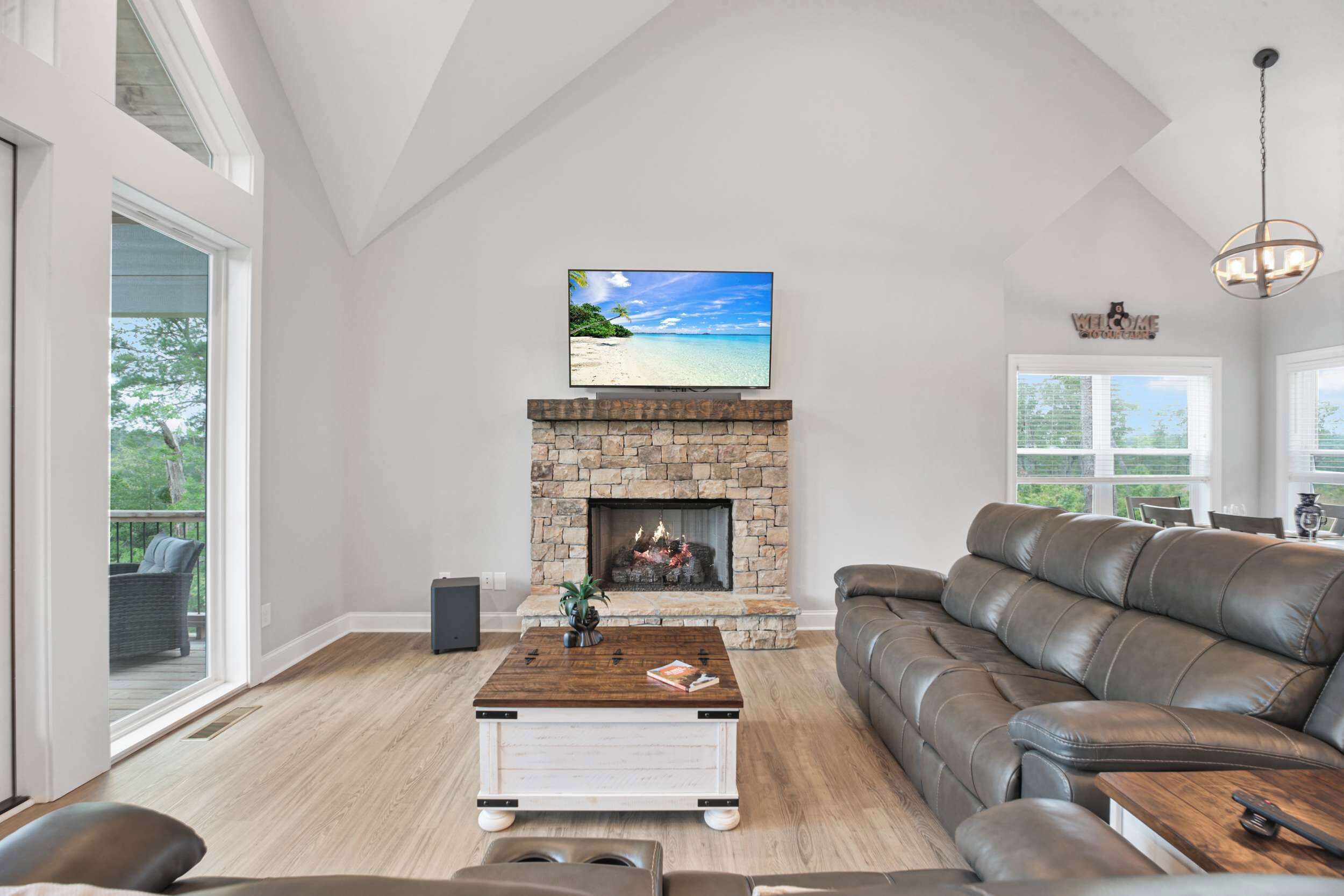 A spacious living room with a stone fireplace, a large flat-screen TV, and a leather sofa.
