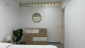 Een slaapkamer met een bed, een houten dressoir, een spiegel en een kamerplant.
