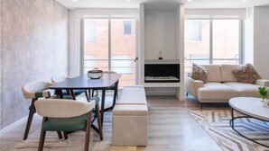 Uma sala de estar moderna com área de jantar, lareira e amplas janelas com vista para a cidade.