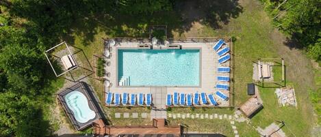 An aerial view of a swimming pool area with a hot tub, lounge chairs, and a wooden deck.
