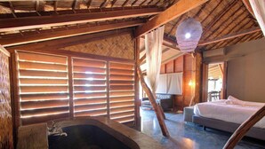 Een rustieke slaapkamer met een houten plafond, een groot bed, een badkuip en een bureau met een stoel.