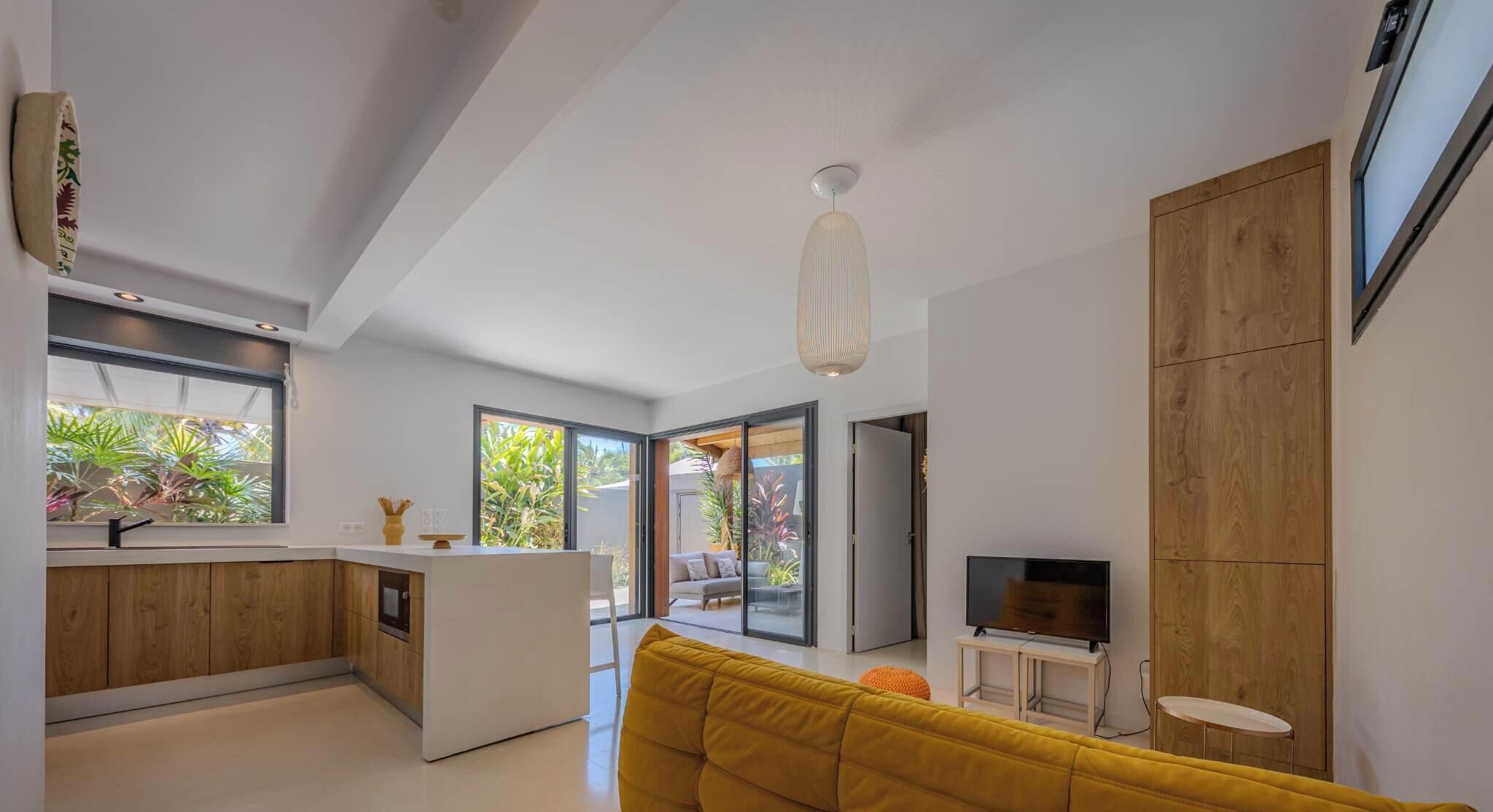A modern kitchen with a central island, a dining area with a sofa, and a TV on a wooden cabinet.