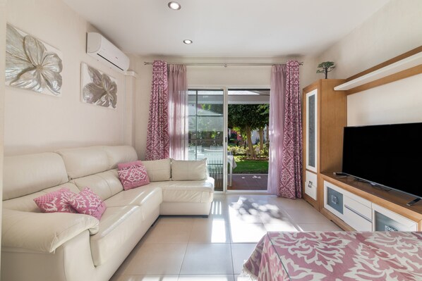 A modern living room with a sofa, TV, and a glass door leading outside.