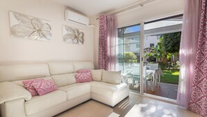 A modern living room with a white leather sofa, decorative wall art, and a sliding glass door leading to an outdoor patio. - Islantilla Golf Holiday Home with Private Terrace, Wi-Fi, and Air Conditioning (Huelva)