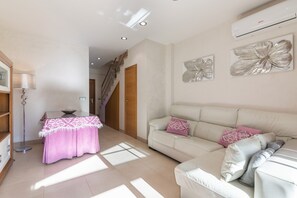 A living room with a sofa, a table with a pink tablecloth, and a staircase.