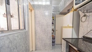 A narrow kitchen with marble tiles, a refrigerator, and a window. - Apartamento na Praia Grande com vista mar (Praia Grande)