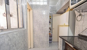 A narrow kitchen with marble tiles, a refrigerator, and a window. - Apartamento na Praia Grande com vista mar (Praia Grande)
