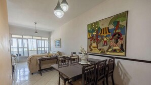 A spacious living area with a dining table, chairs, a sofa, and a large painting on the wall. - Apartamento na Praia Grande com vista mar (Praia Grande)