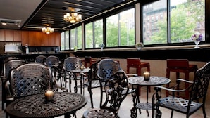 Een restaurantinterieur met hoge plafonds, grote ramen en uitzicht op gebouwen en bomen.