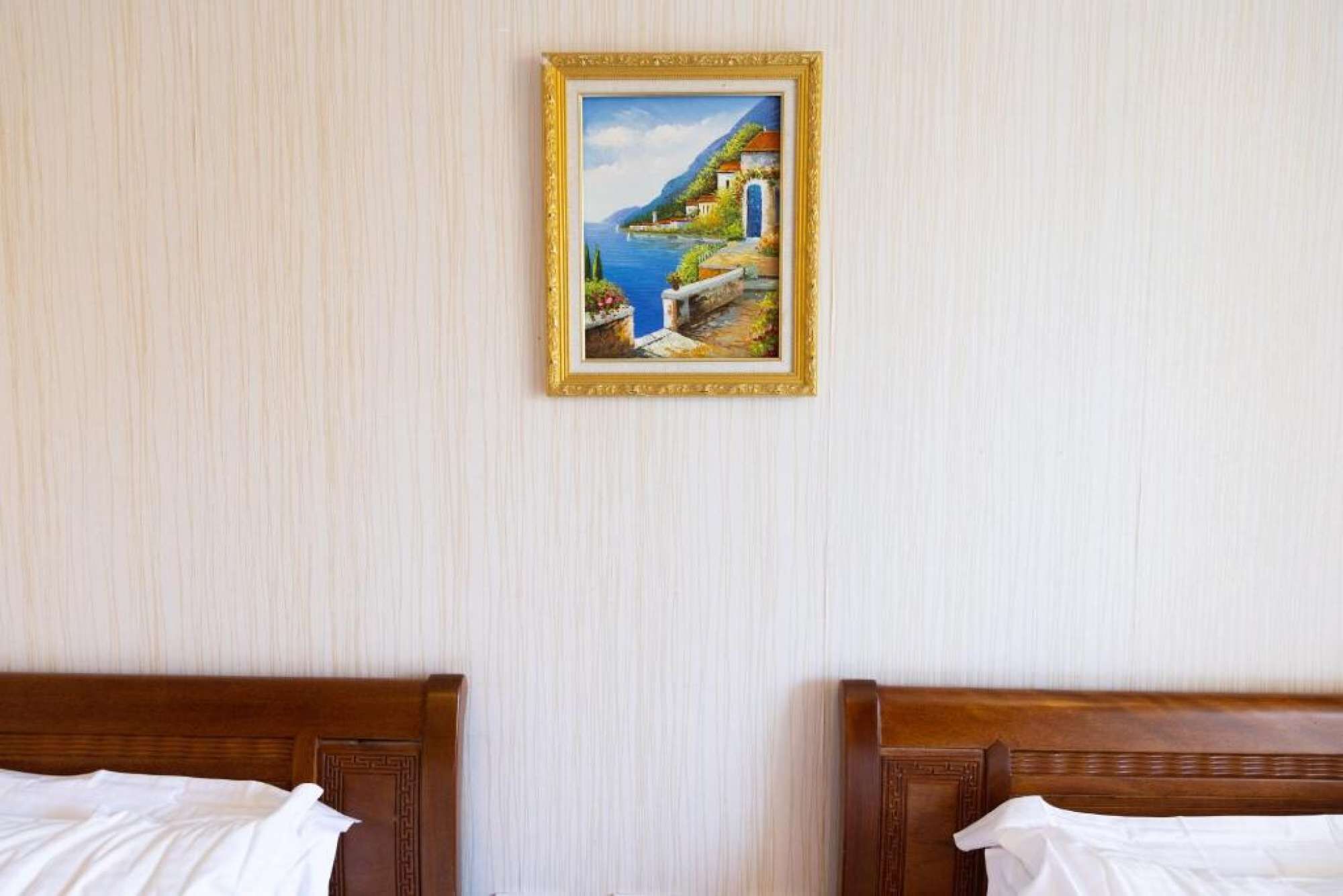 A hotel room with two wooden beds, a framed painting of a coastal scene, and a textured wall.