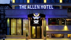 Het uiterlijk van The Allen Hotel, met een opvallend verlicht bord, grote ramen en een goed verlichte entree.