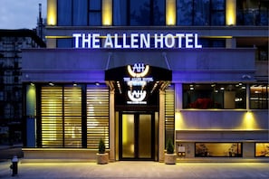 Exterior del Hotel Allen, con una entrada destacada, ventanas amplias y fachada bien iluminada.