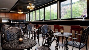 Een restaurantinterieur met hoge plafonds, grote ramen en uitzicht op gebouwen en bomen.