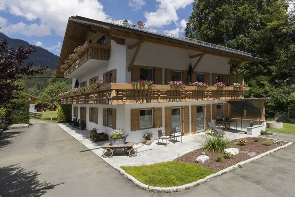 A two-story chalet with wooden balconies, a patio area with outdoor seating, and a view of the surrounding forest. - Apartment in Grainau am Badersee (Grainau)
