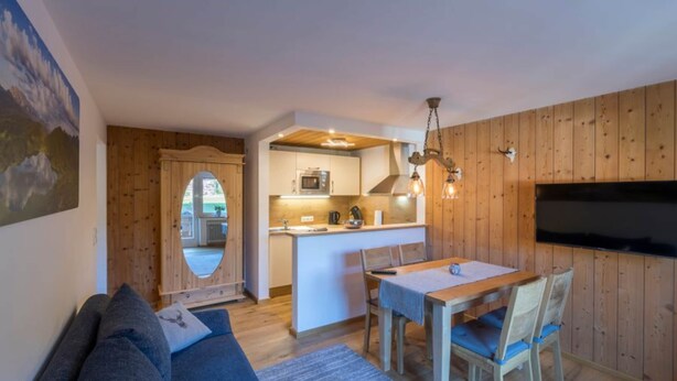 A cozy living room with a sofa, a dining table with chairs, a kitchen area with a microwave, and a TV mounted on the wall. - Apartment in Grainau am Badersee (Grainau)