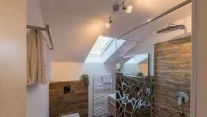 A modern bathroom with a skylight, a shower with a glass enclosure, a wooden accent wall, and a white toilet. - Apartment in Grainau am Badersee (Grainau)