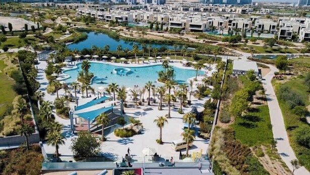 Un complexe hôtelier doté d’une grande piscine centrale, entourée de palmiers et de promenades.