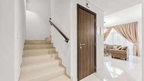 Un intérieur moderne avec un escalier, une porte en bois, un canapé beige et une grande fenêtre avec des rideaux.