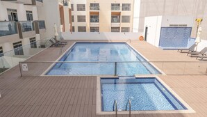 Piscina en la azotea con dos zonas diferenciadas, rodeada por una terraza de madera y barandillas de cristal.
