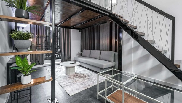 Un espacio habitable moderno con una escalera de cristal, un sofá gris y una mesa de centro.