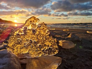 A large, irregularly shaped rock formation on a beach with the sun setting in the background. - Seaside Apartment | Pool, Sauna, Parking, Balcony (Kołobrzeg)