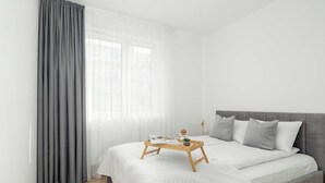 A modern bedroom with a large bed, grey curtains, and a wooden bedside table with a tray. - Modern Apartment | Private Parking and Balcony (Poznań)