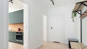 A modern kitchen with green cabinets and a wooden countertop, a white door, and a bench with a metal frame. - Modern Apartment | Private Parking and Balcony (Poznań)