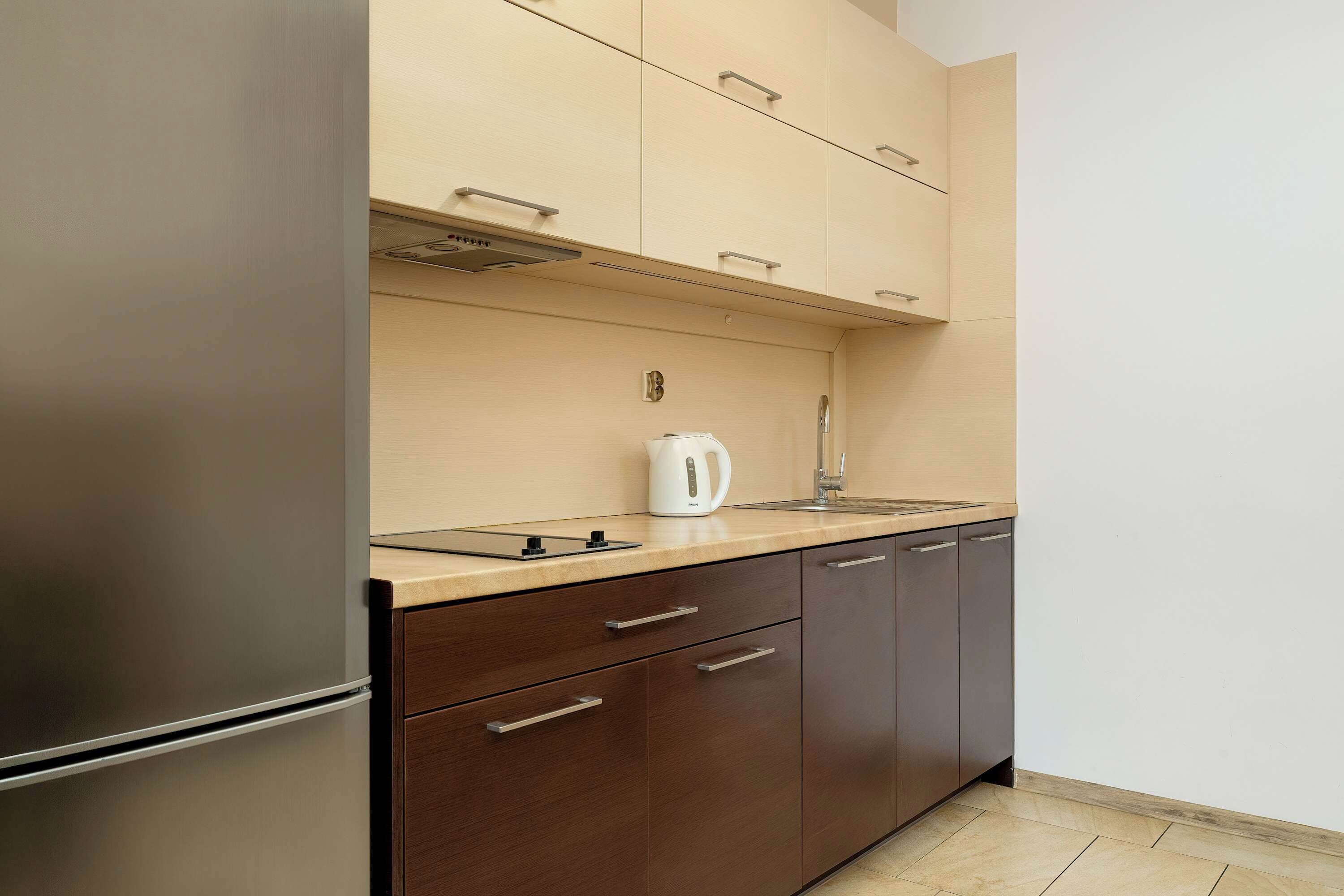 A modern kitchen with a stainless steel refrigerator, wooden cabinets, a countertop, and a kettle.