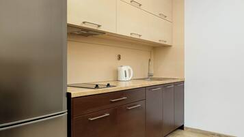 A modern kitchen with a stainless steel refrigerator, wooden cabinets, a countertop, and a kettle.