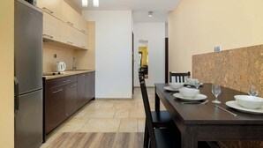 Una cocina moderna con armarios oscuros, un refrigerador de acero inoxidable y un comedor con una mesa de madera oscura para dos.