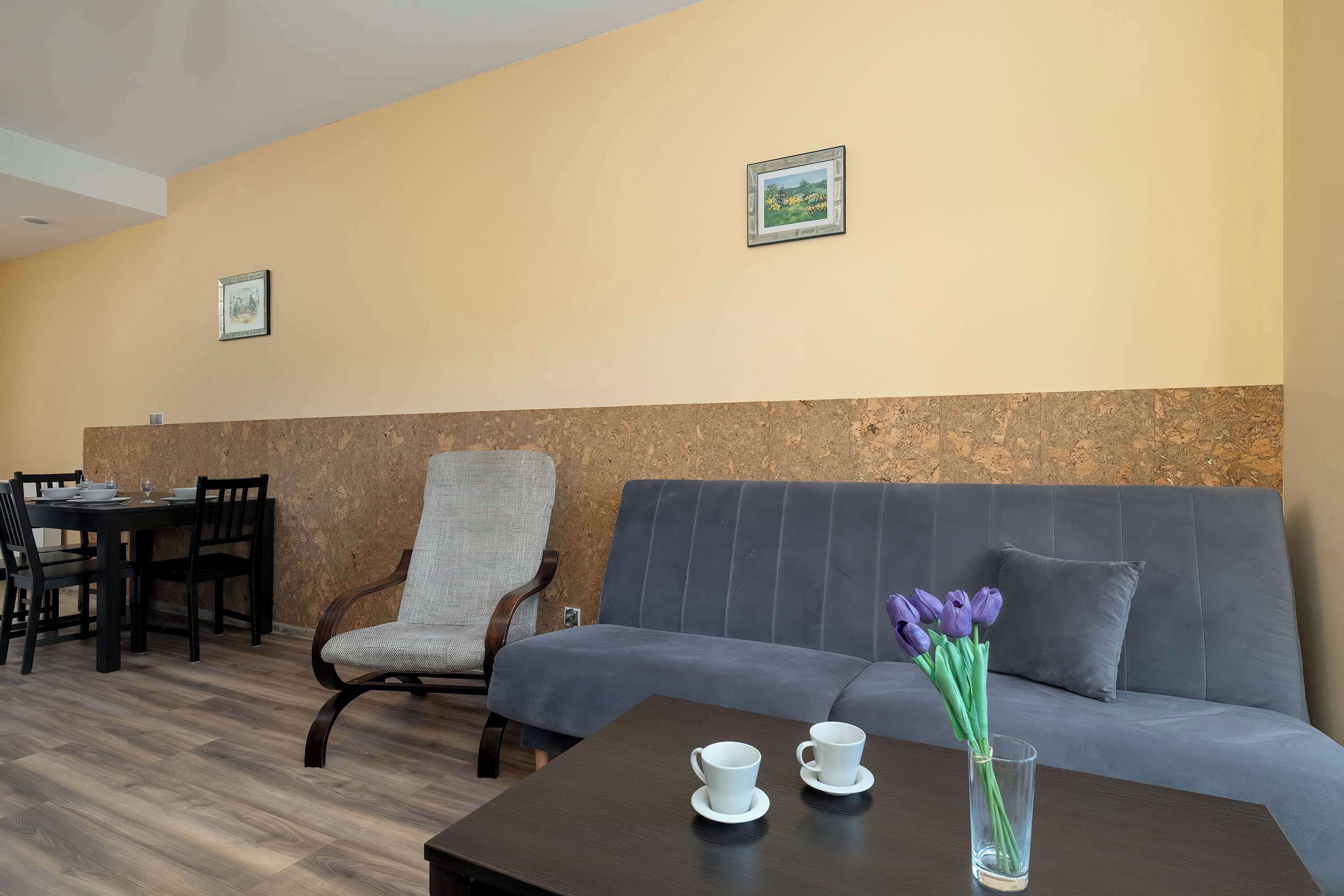 Une pièce moderne comprenant un canapé, une table à manger avec des chaises, et une petite table sur laquelle se trouvent des tasses et un vase de fleurs.