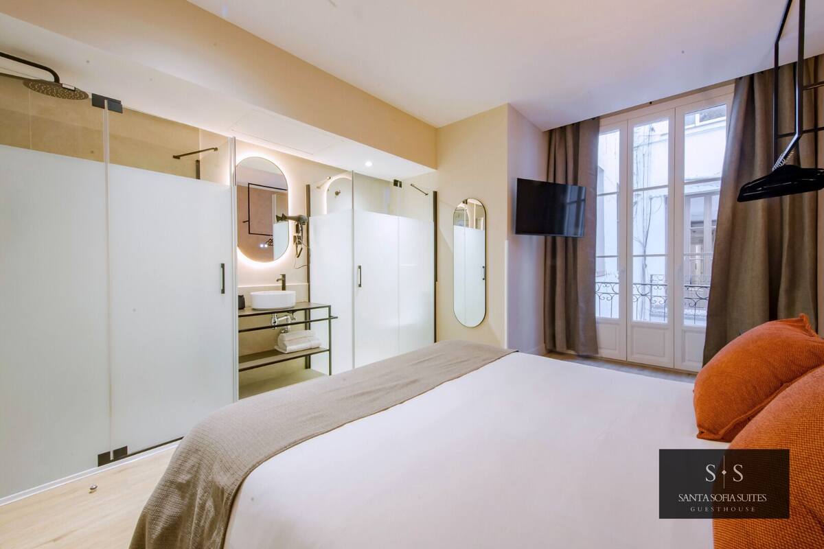 A modern hotel room with a large bed, a vanity with a mirror, a TV, and a balcony view.