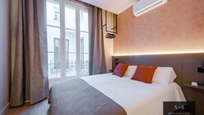 Ein Hotelzimmer mit einem großen Bett, einem Nachttisch, einer Wand-Klimaanlage und Blick auf die Stadt durch das Fenster.