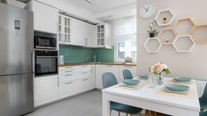 A modern kitchen with white cabinets, a built-in oven, and a dining area with teal chairs and a white table.