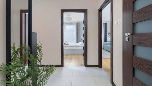 A hallway leading to a bedroom with a bed, a bedside table, and a window with curtains.