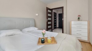 A neatly made bed with a tray of items, a bedside table with a vase, and a dresser with drawers.