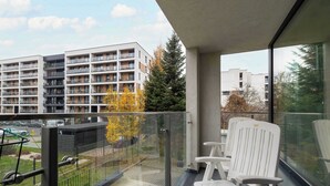 A balcony with a glass railing, white chairs, and a view of a multi-story building with balconies.