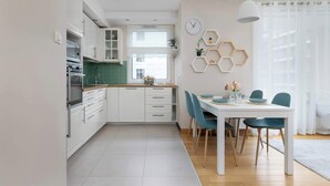 A modern kitchen with white cabinets, a dining area with a white table and teal chairs, and a hexagonal shelf with decorative items.