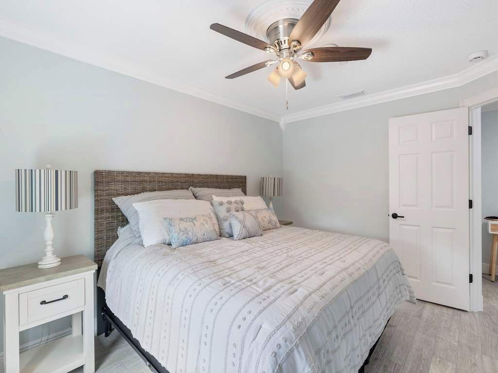 Un dormitorio con una cama, una mesita de noche, un ventilador de techo y una puerta.
