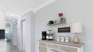 Un couloir avec une console en bois, une machine à café, des tasses et un panneau indiquant « Bar à café et à vin ».