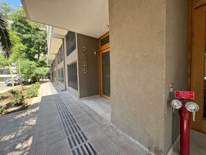 Entrada d'un edifici amb el número '2505' a la paret, un hidrant vermell i un cel serè.