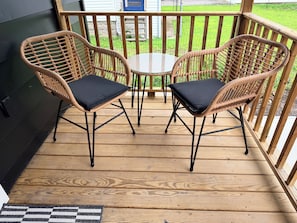 Eine Holzterrasse mit zwei Korbstühlen und einem kleinen Tisch.
